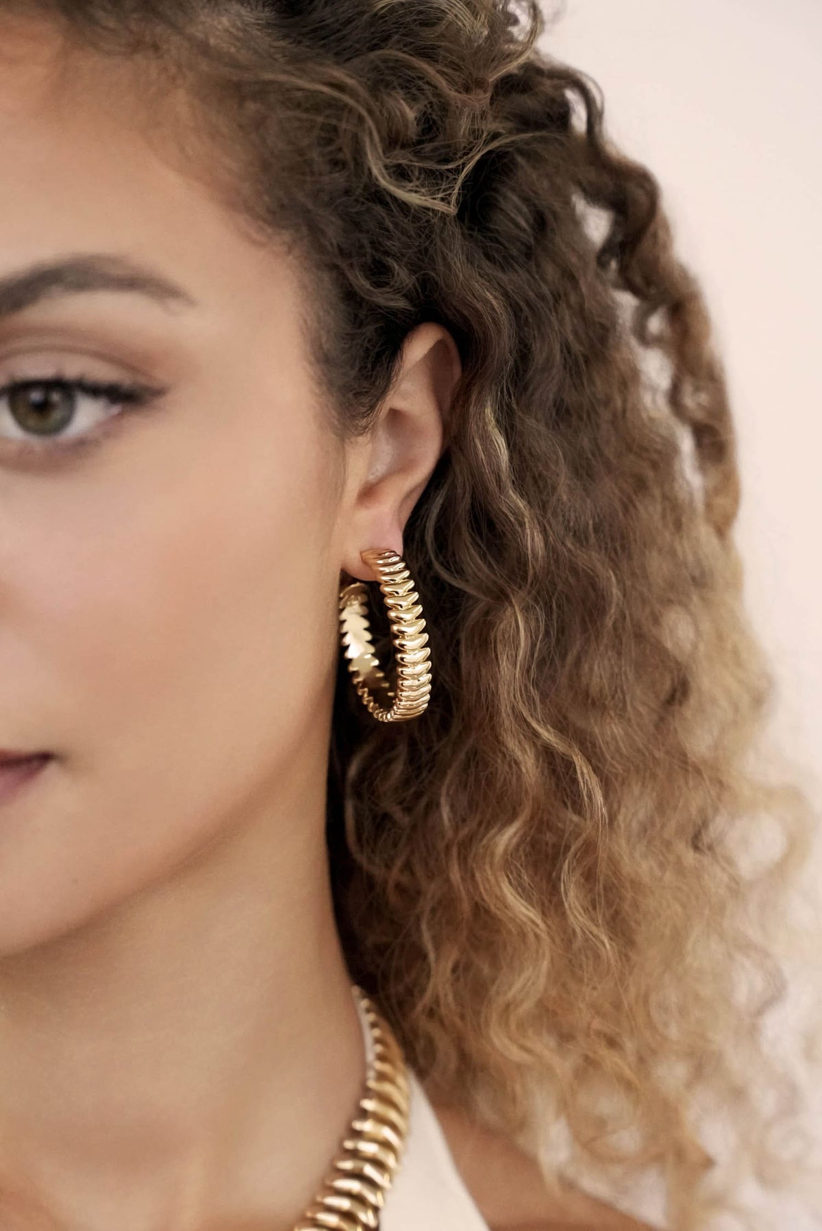 Close-up of a person wearing gold hoop earrings with a neutral background