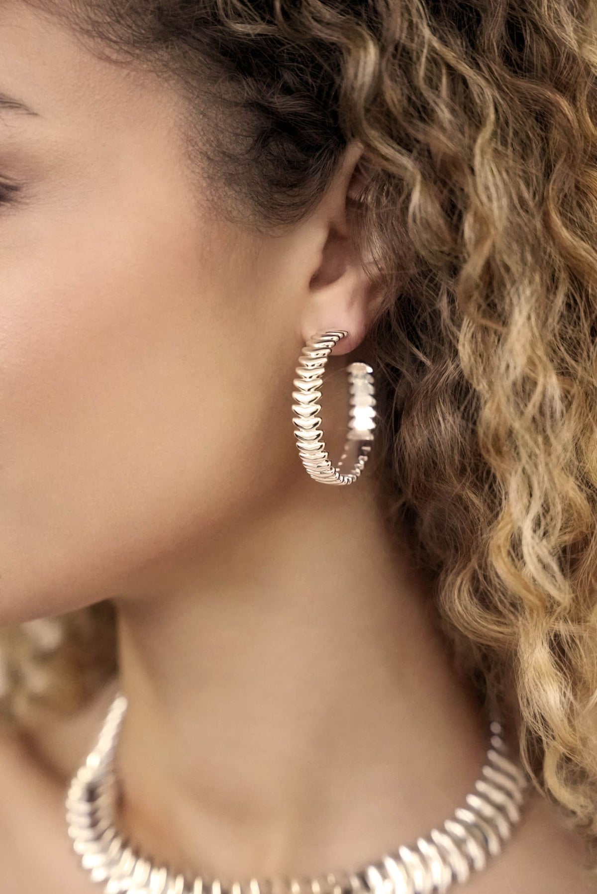 Close-up of a person wearing gold hoop earrings with a blurred background