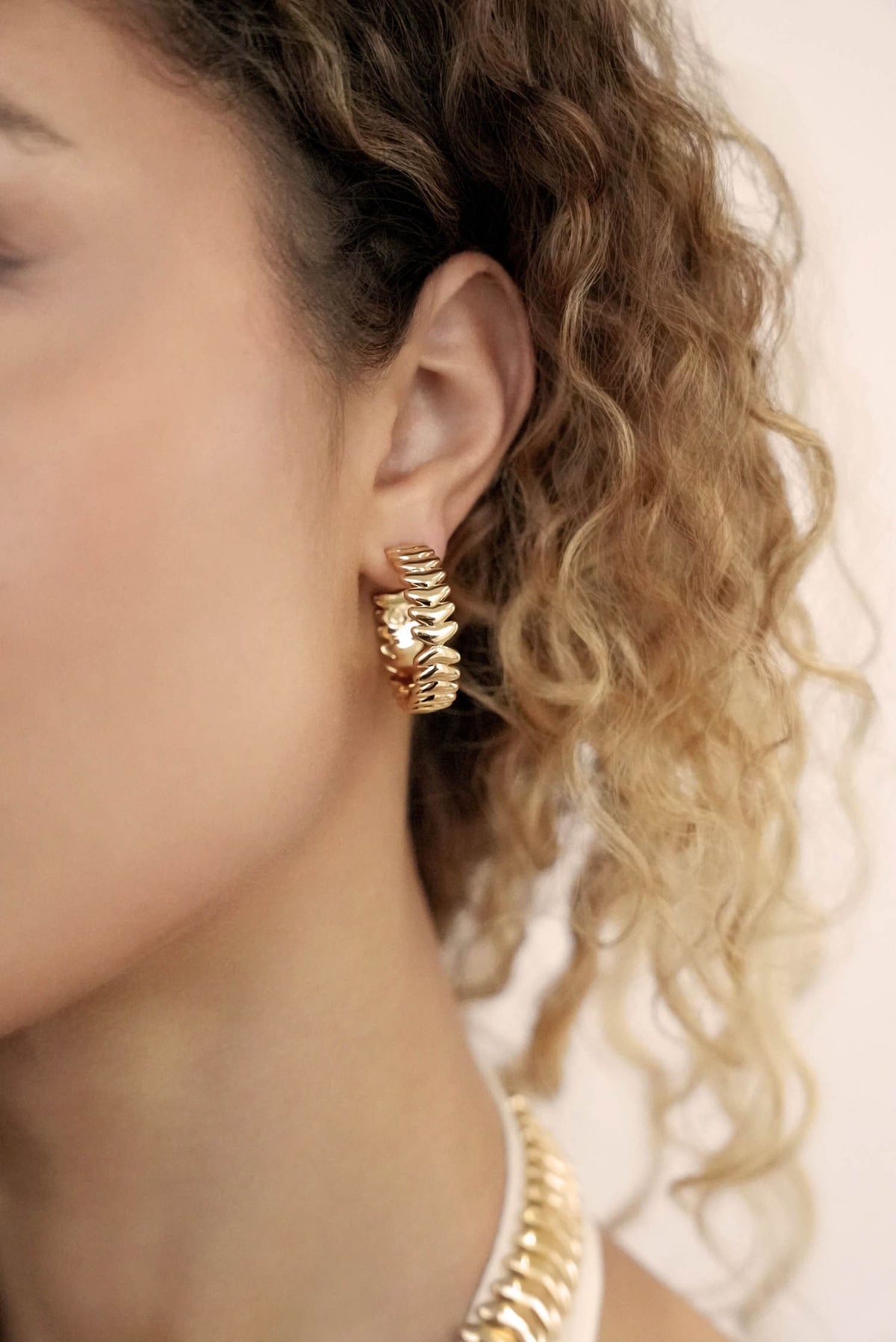 Close-up of a person wearing gold hoop earrings with a blurred background