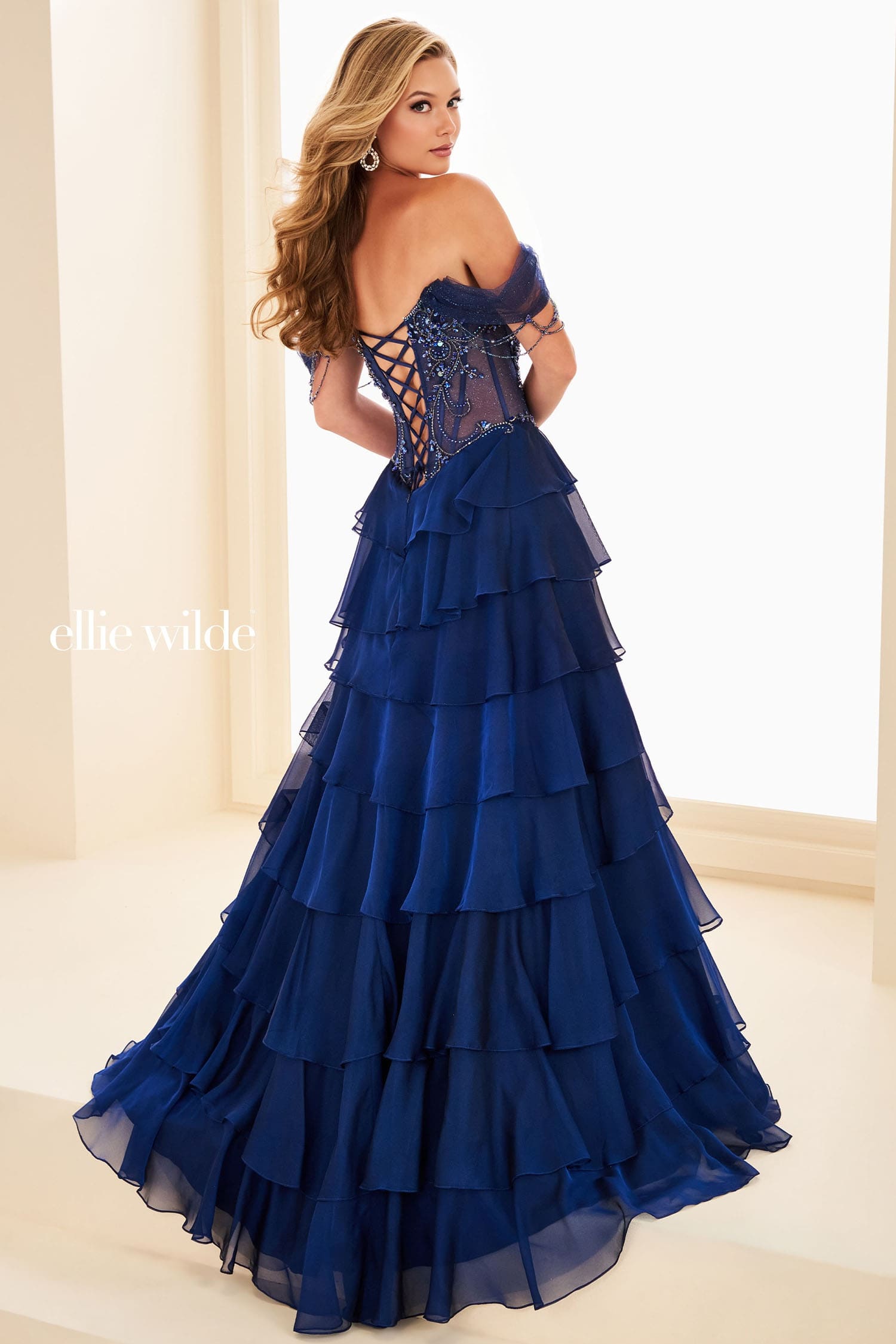 Woman wearing a blue evening gown with ruffled layers, standing indoors.