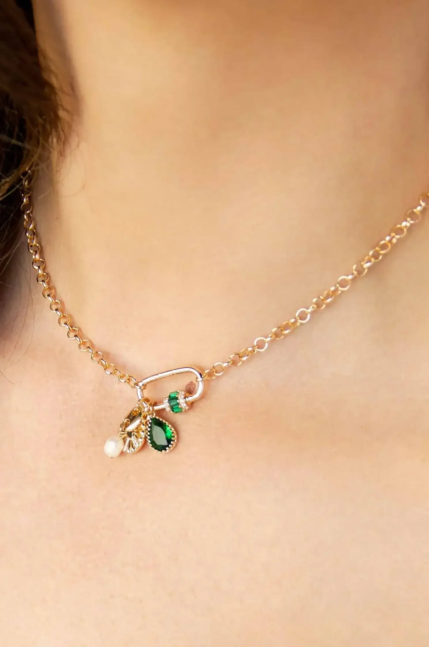 A delicate gold chain necklace adorned with colorful charms, including green and pearl accents, rests on a smooth, light-skinned neck, highlighting a subtle and elegant style.