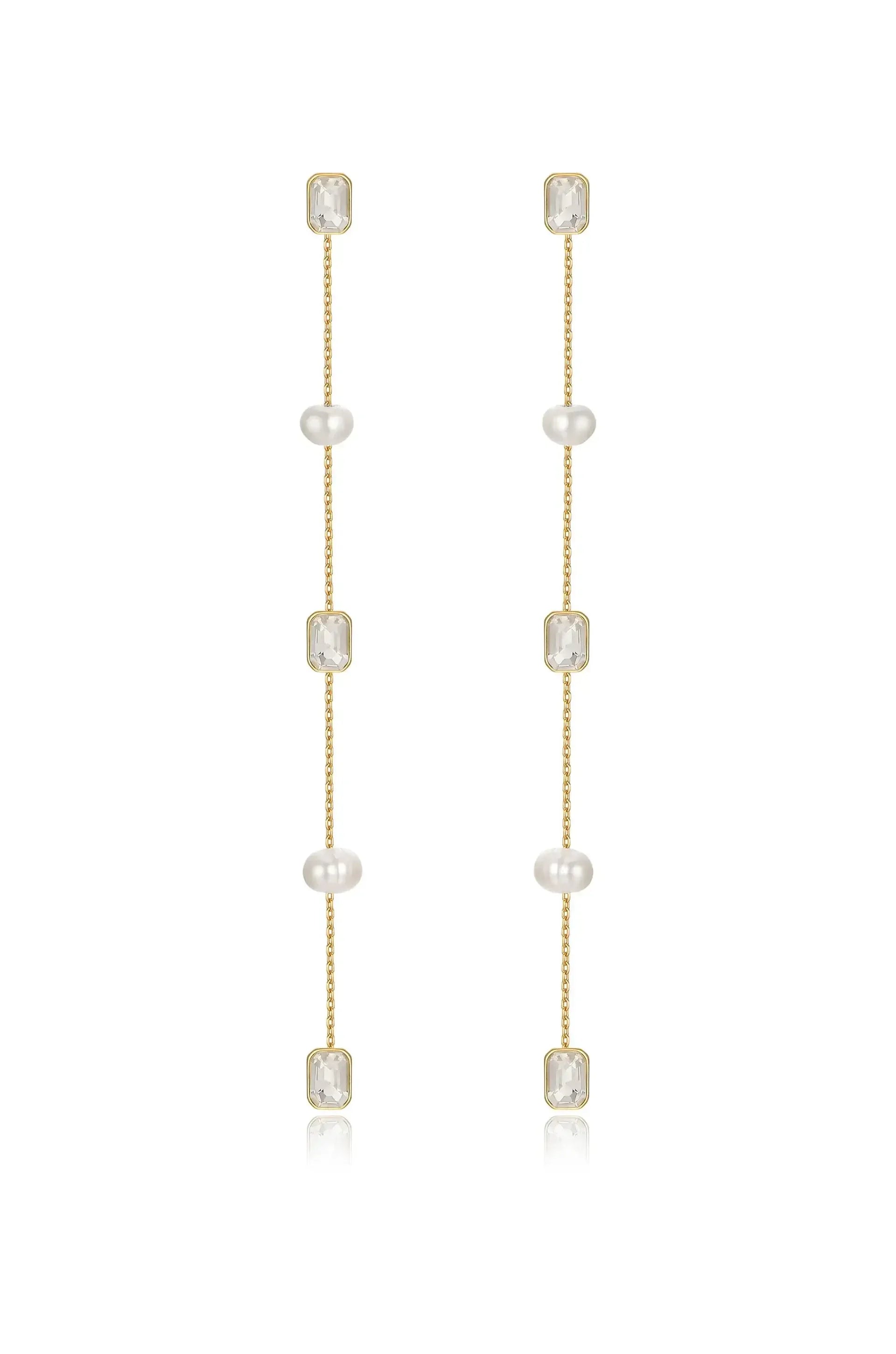 Gold earrings feature four pearl beads and two rectangular clear stones, hanging delicately in a vertical arrangement, reflecting light against a neutral backdrop.