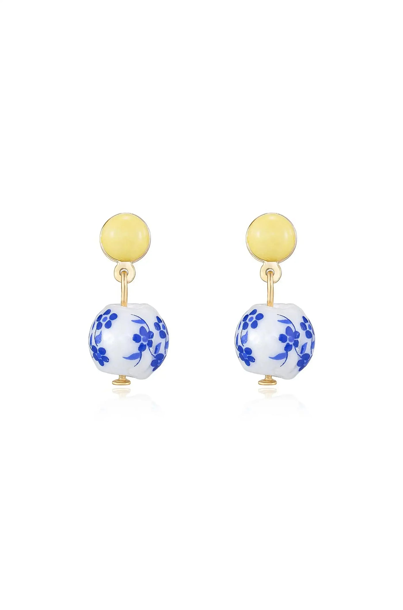 Gold-tone earrings feature a yellow circular top with a blue floral-patterned porcelain ball dangling below. They appear on a reflective surface, highlighting their design and materials.