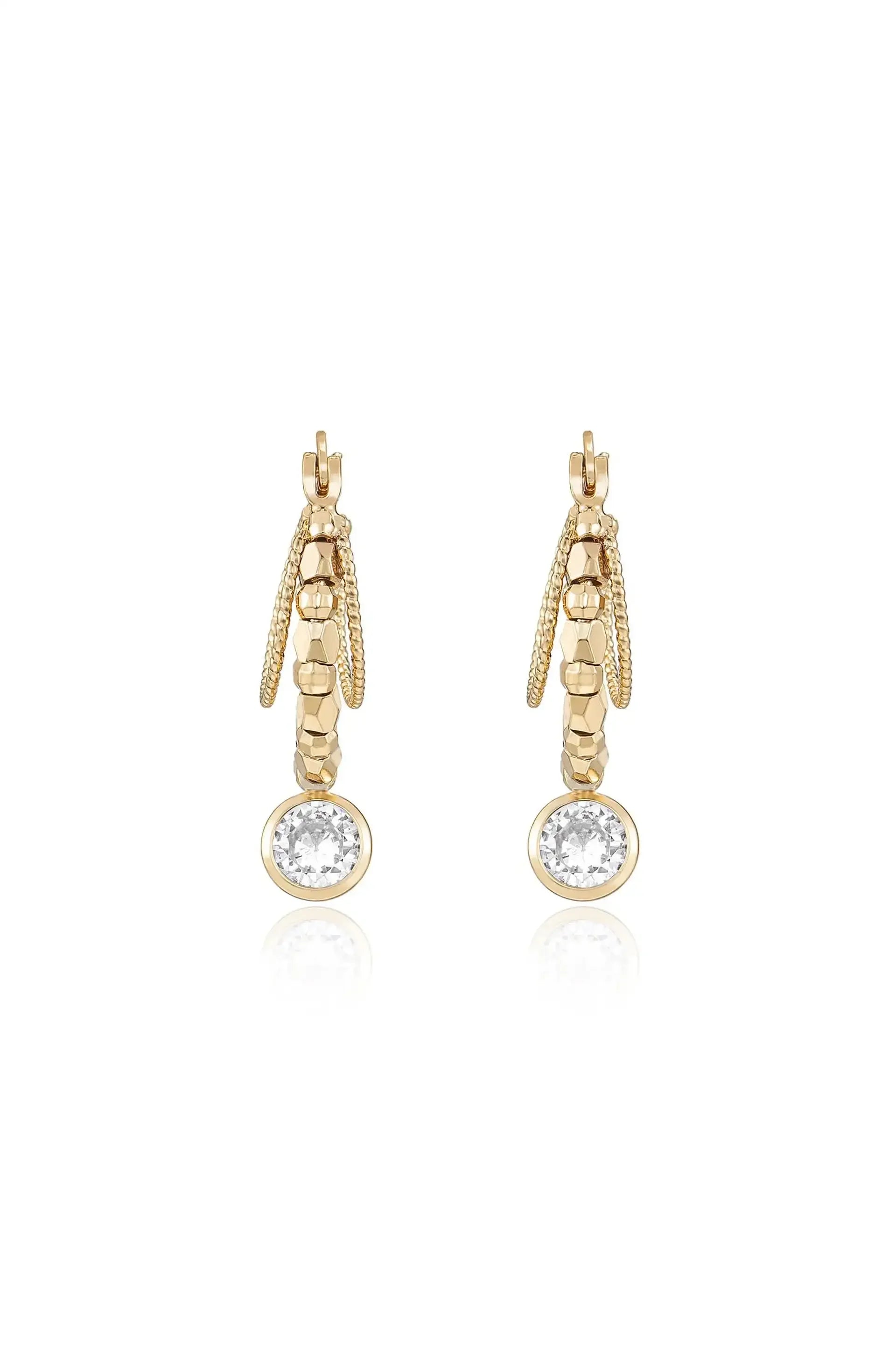 Gold earrings are displayed, featuring a textured design with a round, sparkling stone at the bottom. The setting is reflective, enhancing their elegant appearance.
