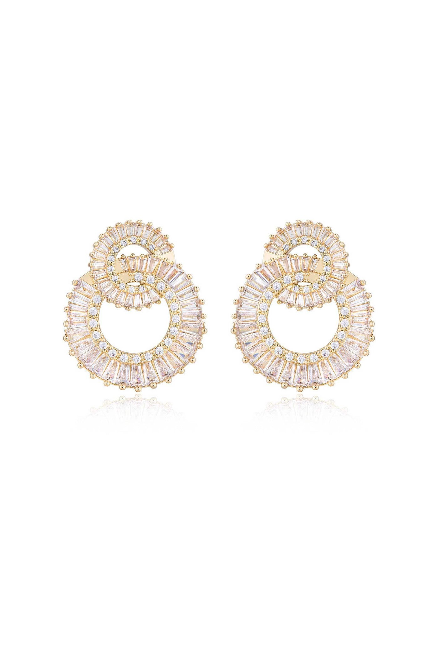 Golden hoop earrings with intricate patterns feature a spiral design filled with sparkling gemstones. They are displayed on a reflective surface, enhancing their elegance and shine.