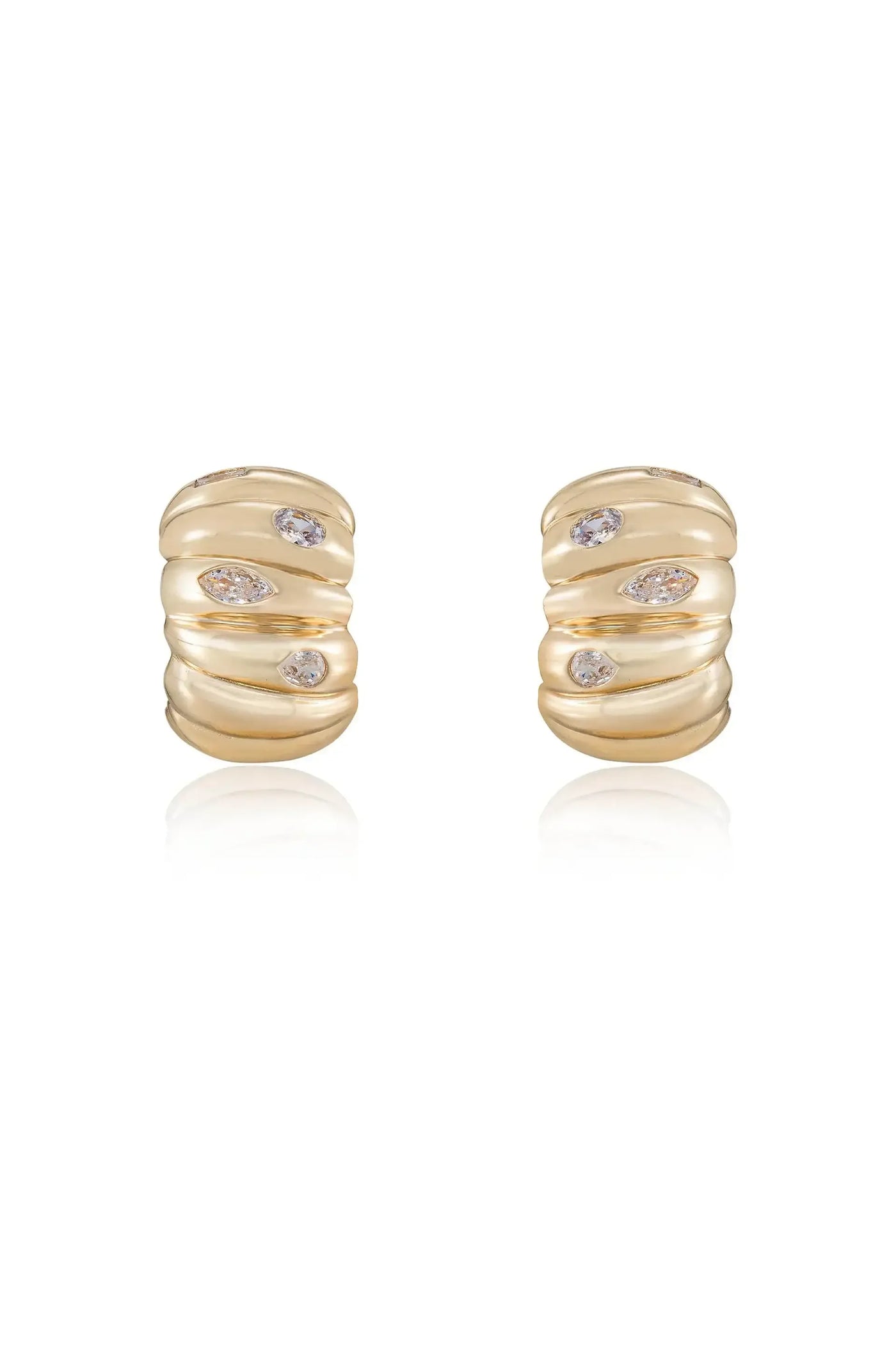 Two gold earrings, featuring a wavy design with scattered, sparkling gemstones. They rest on a reflective surface, enhancing their elegant appearance.