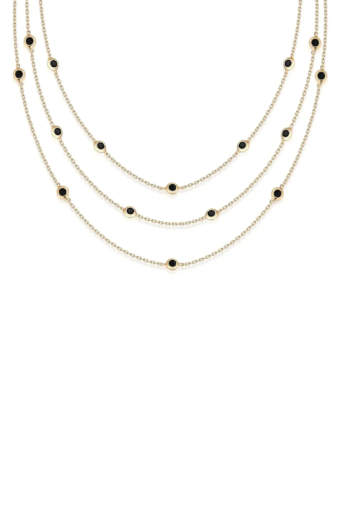 A layered gold necklace featuring multiple chains, adorned with evenly spaced circular black stones, elegantly drapes against a plain white background.