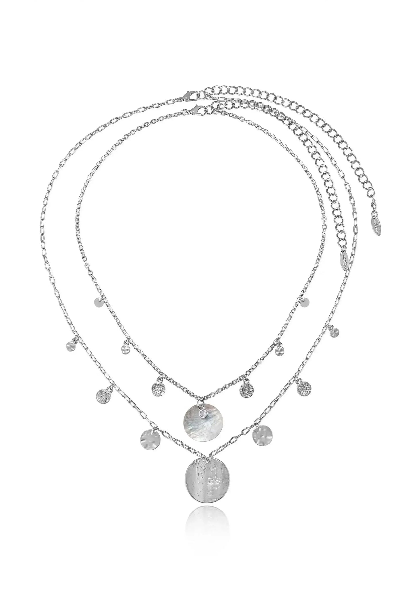 A delicate silver necklace features multiple interlinked chains adorned with various small, shimmering pendants and a larger, textured circular charm, reflecting light against a neutral background.