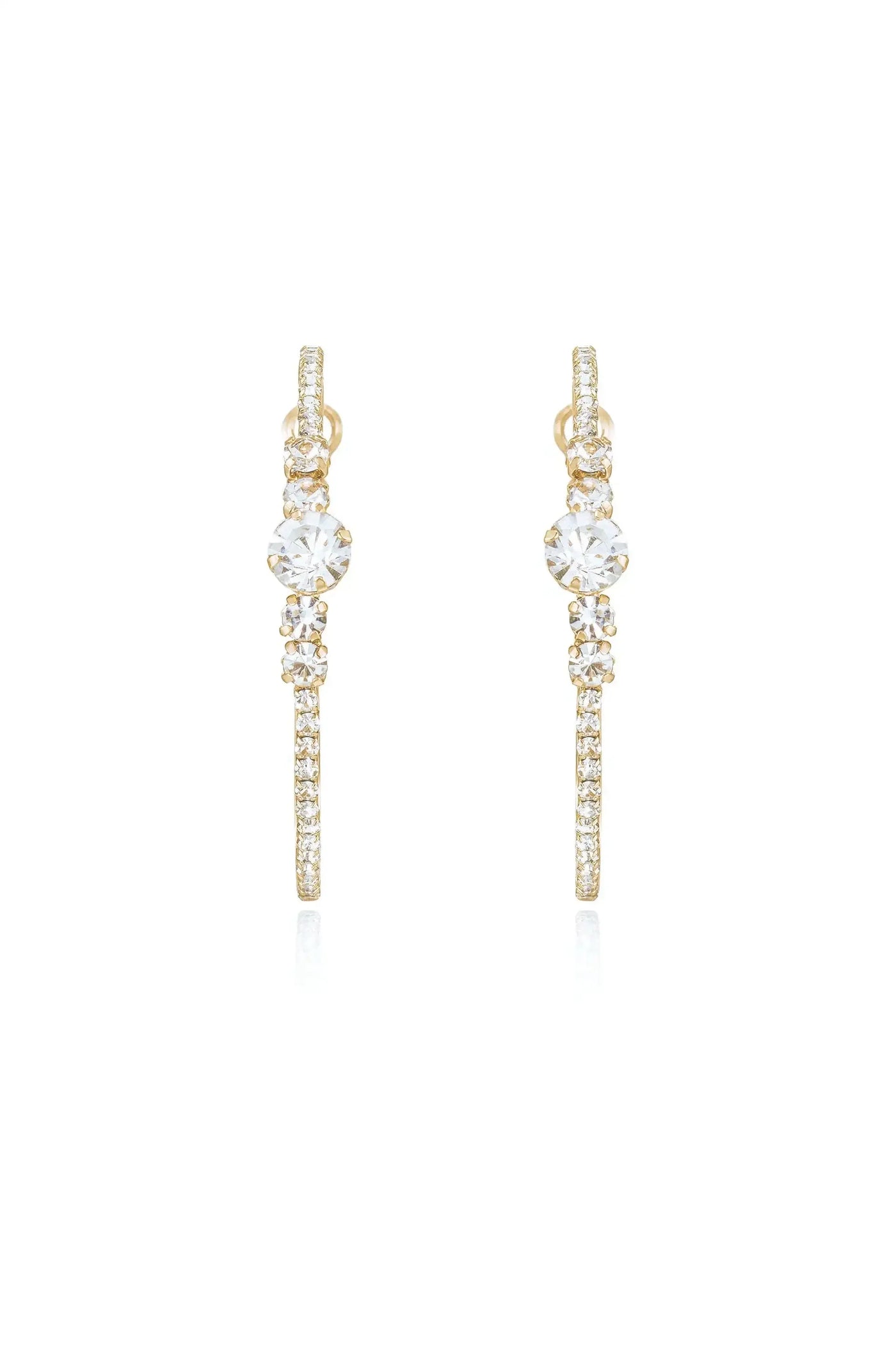 Gold earrings adorned with sparkling crystals hang vertically, catching light and reflecting it. They are displayed against a white background, emphasizing their elegance and shine.