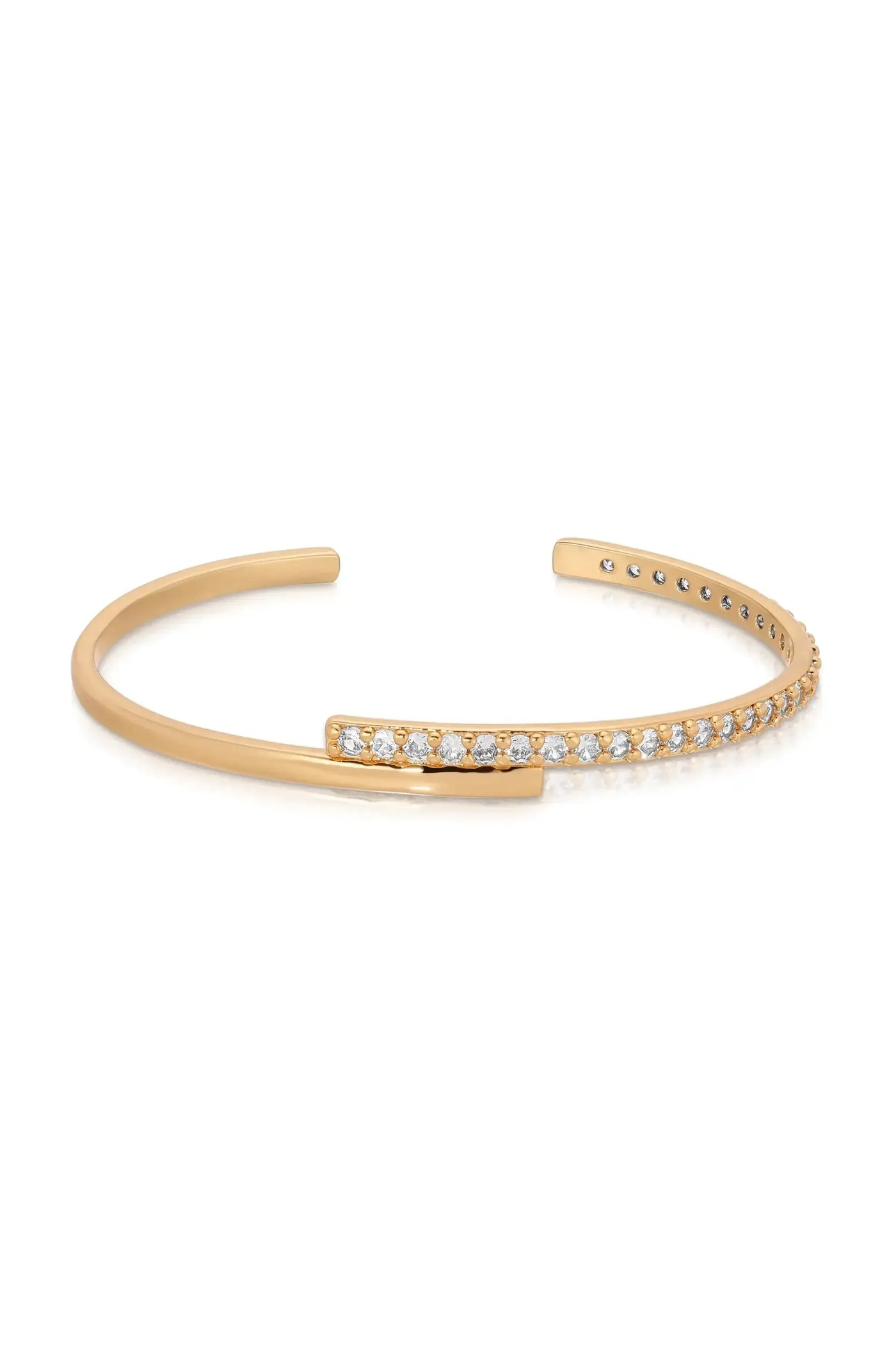 A gold cuff bracelet features a sleek design with one end adorned by a row of small, sparkling stones, resting on a reflective surface.