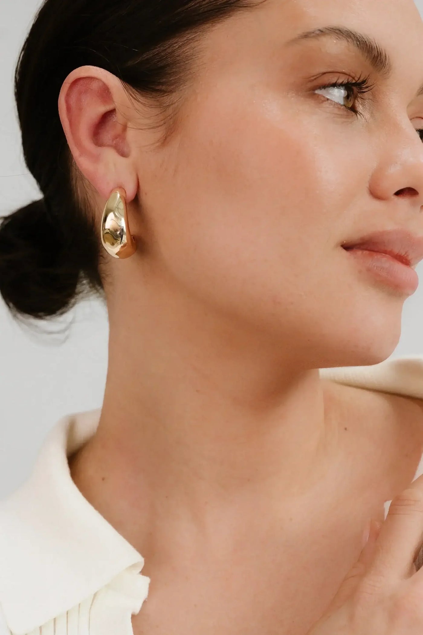 A woman with a smooth complexion and subtle makeup wears large gold earrings. She gazes slightly to the side, highlighting her elegant features against a neutral background.