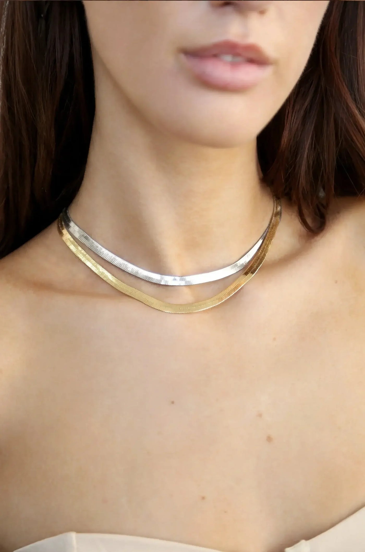 A close-up of a neck features a layered necklace composed of silver and gold metallic strands, resting gracefully on a smooth, bare collarbone, accentuating a natural skin tone.