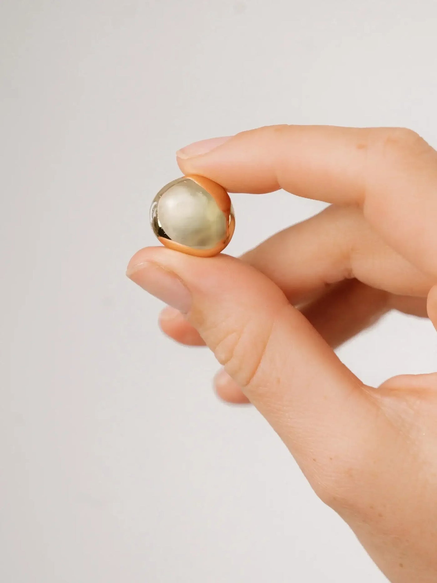 A hand holds a small, glossy spherical object, showcasing its shiny surface. The background is a soft, neutral tone that emphasizes the object being examined.