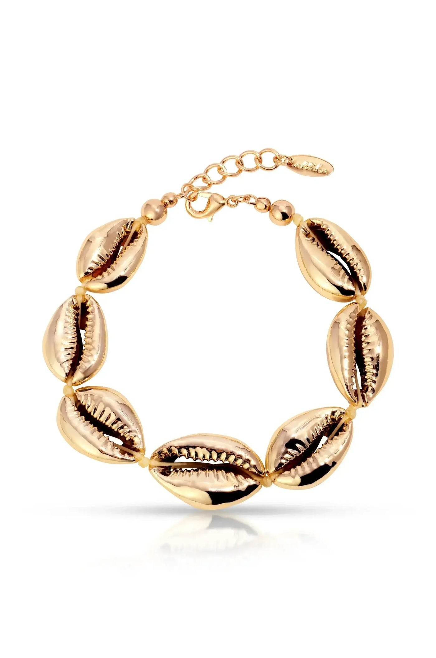 A gold bracelet features a series of shiny cowrie shell motifs, connected by small beads, with an adjustable chain for size. It rests on a reflective surface.