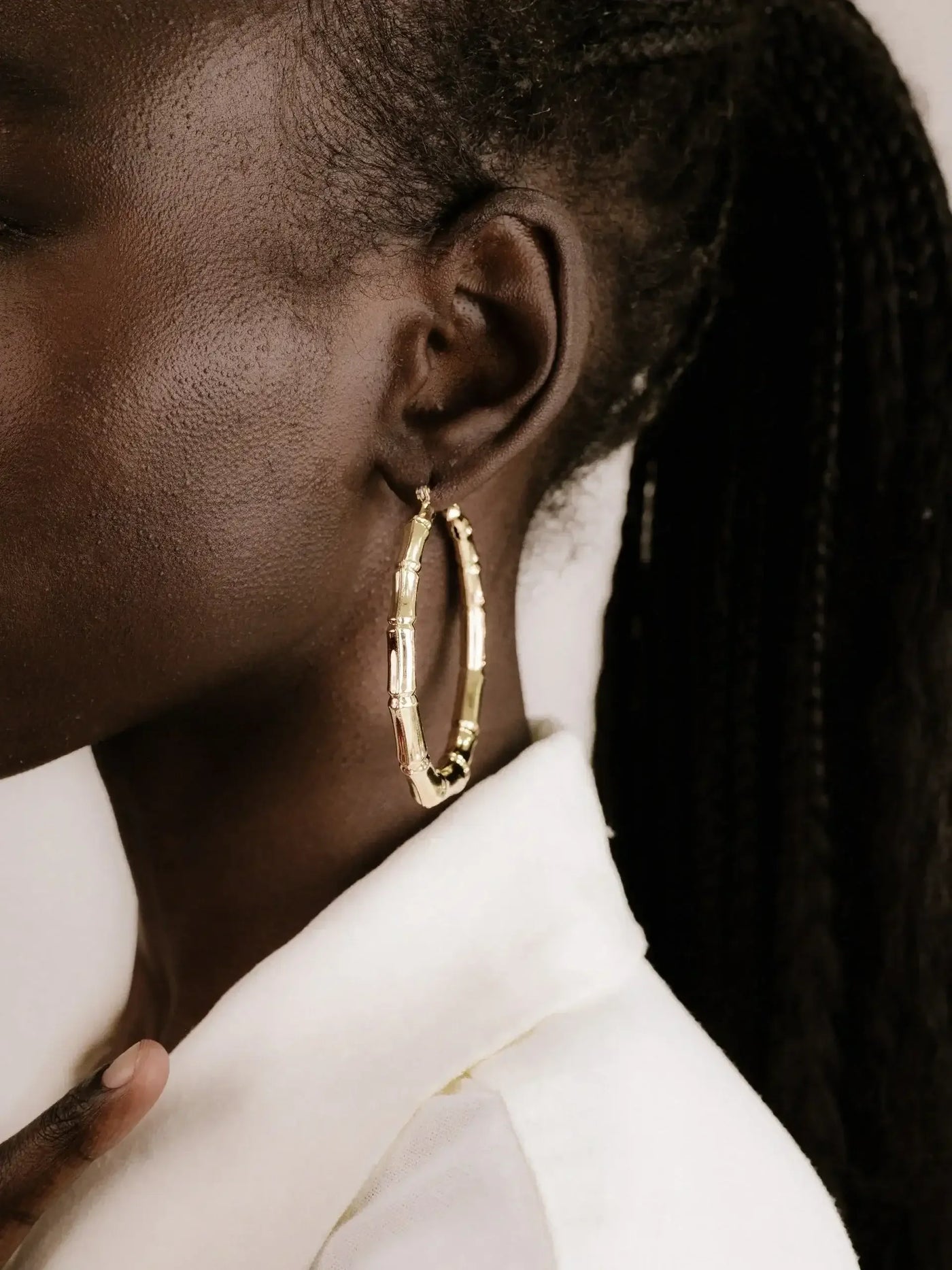 A close-up of a person's ear adorned with a large, golden hoop earring. The individual is wearing a white collar shirt, with a textured background enhancing the focus on the jewelry.