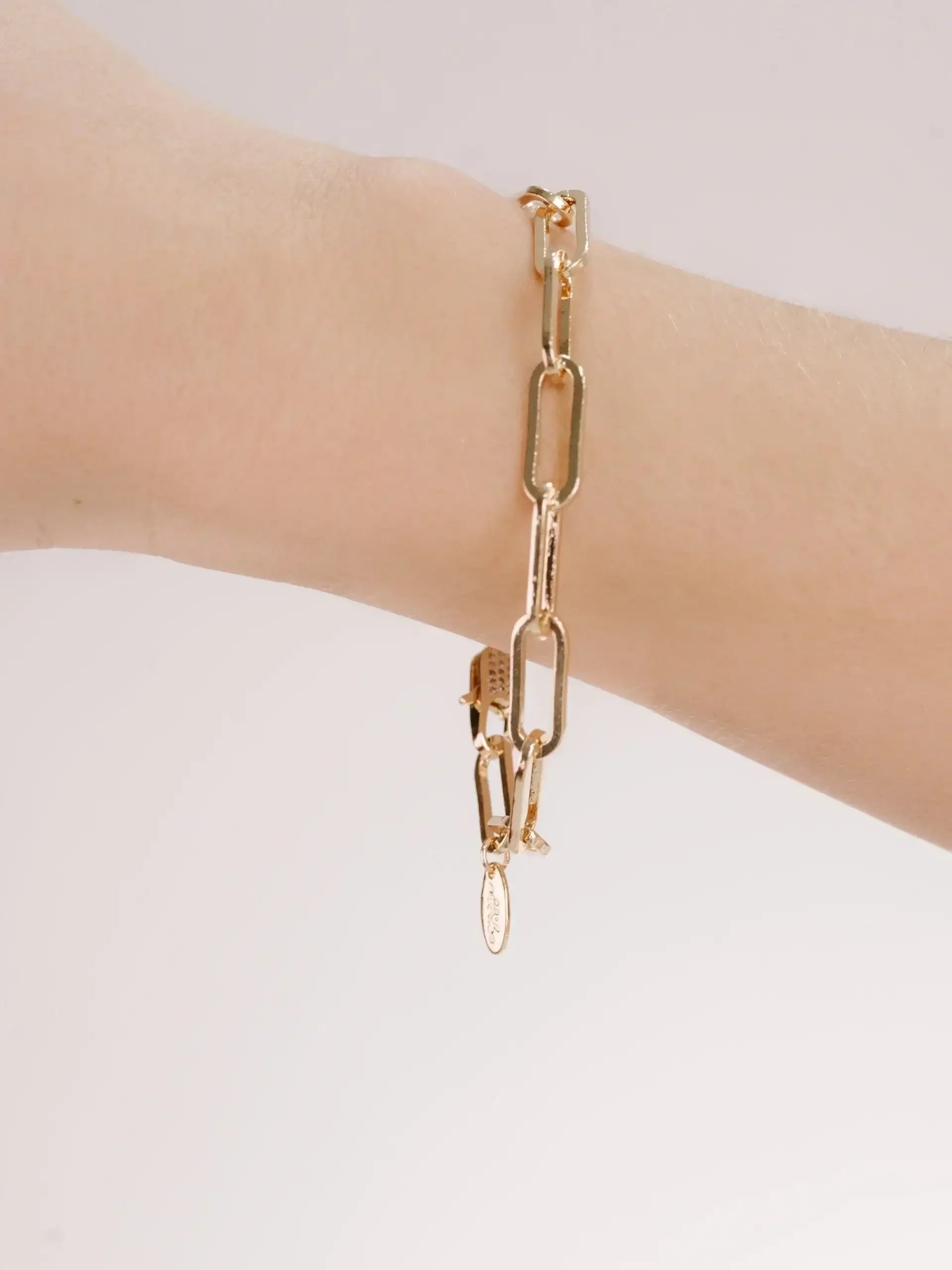 A gold chain bracelet is displayed on a wrist, showcasing its elongated links. The background is light and minimal, emphasizing the bracelet's design and shine.