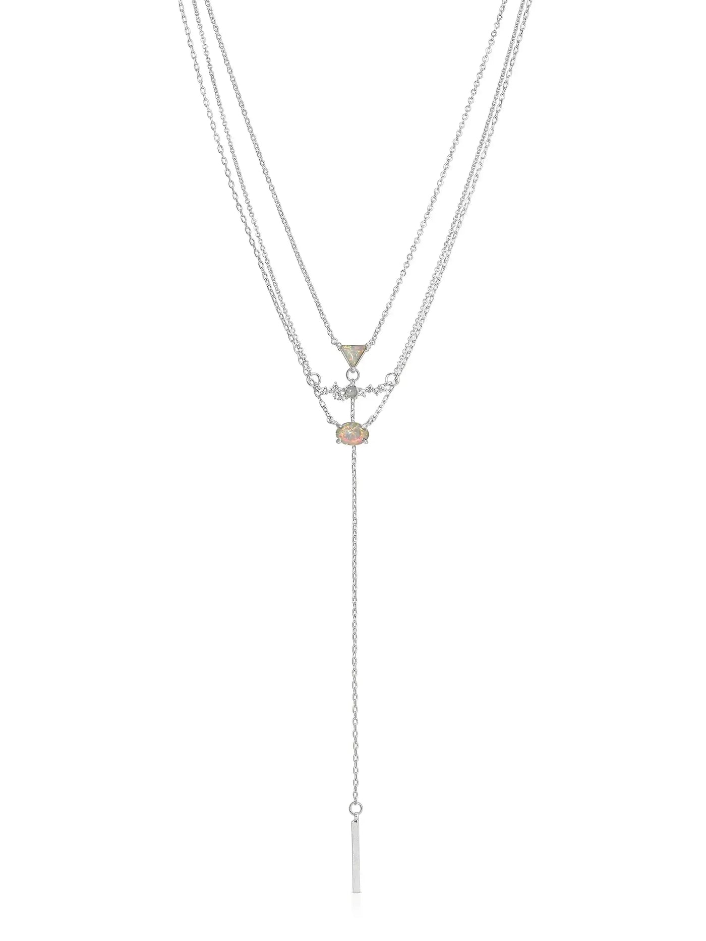 A layered silver necklace features a central colored gemstone and geometric pendants, with a long, delicate chain ending in a thin bar, displayed against a plain white background.