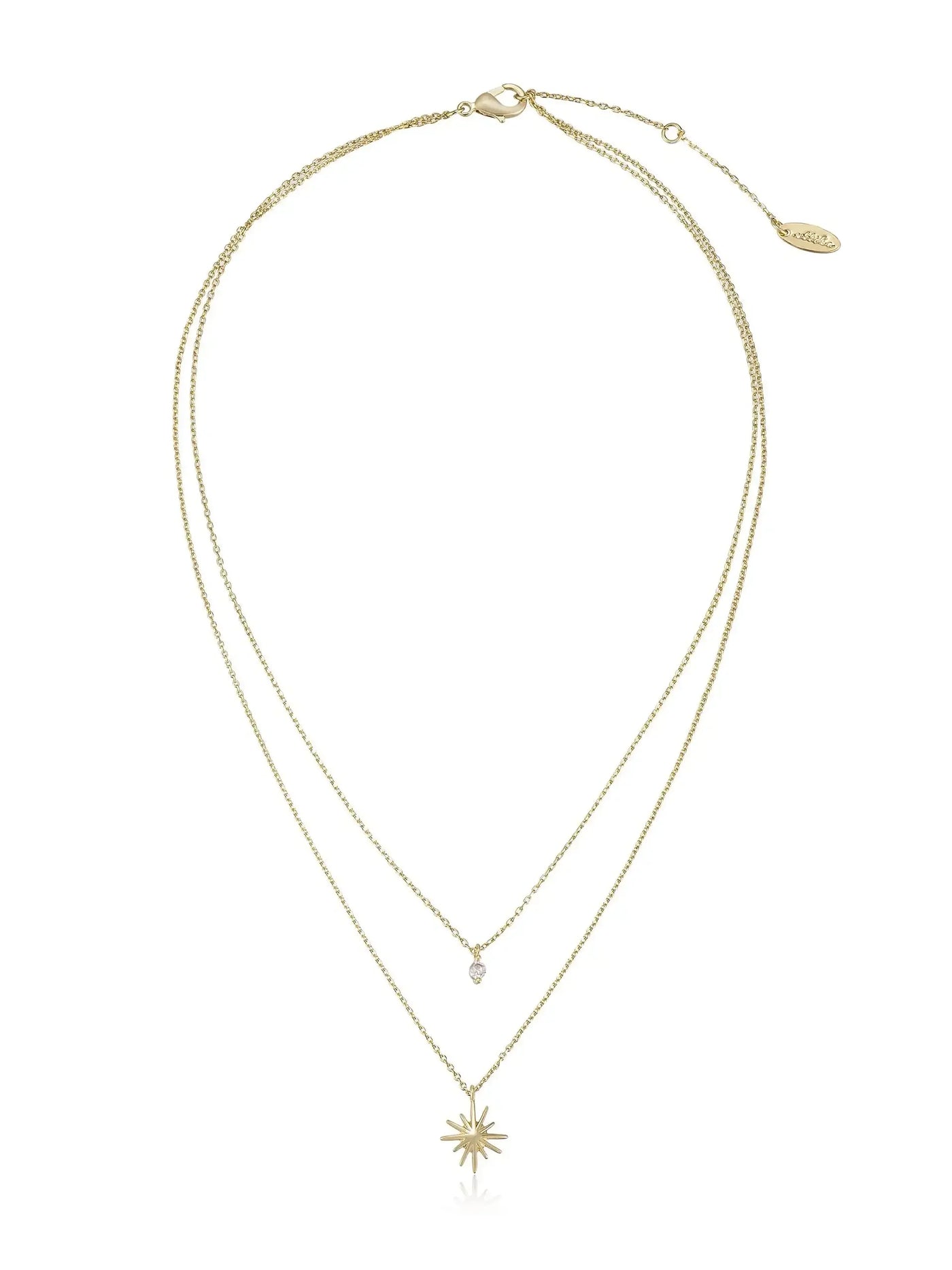 A gold necklace with two chains: one short with a diamond-shaped pendant, and a longer chain featuring a starburst pendant, displayed against a plain white background.