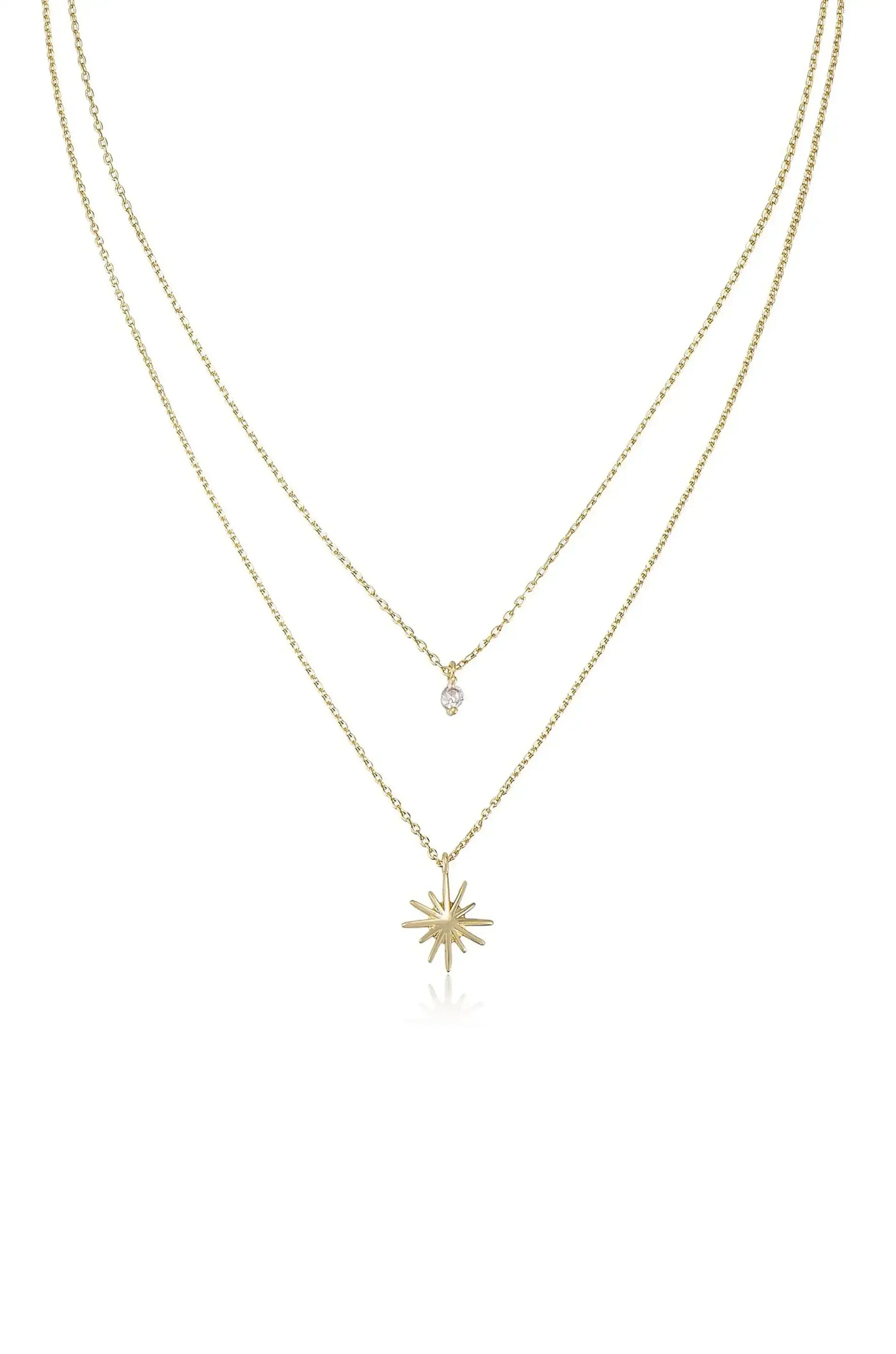 A gold necklace features two chains, one with a small sparkling stone and the other with a star-shaped pendant, displayed against a plain white background.