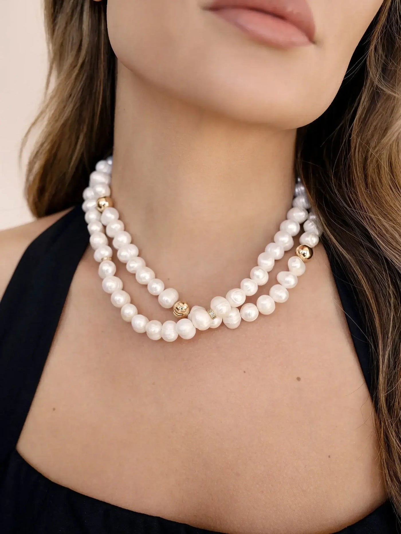 A multi-strand pearl necklace is draped around the neck of a woman, accentuating her collarbone. The setting is minimalistic, focusing on the jewelry and her smooth skin tone.