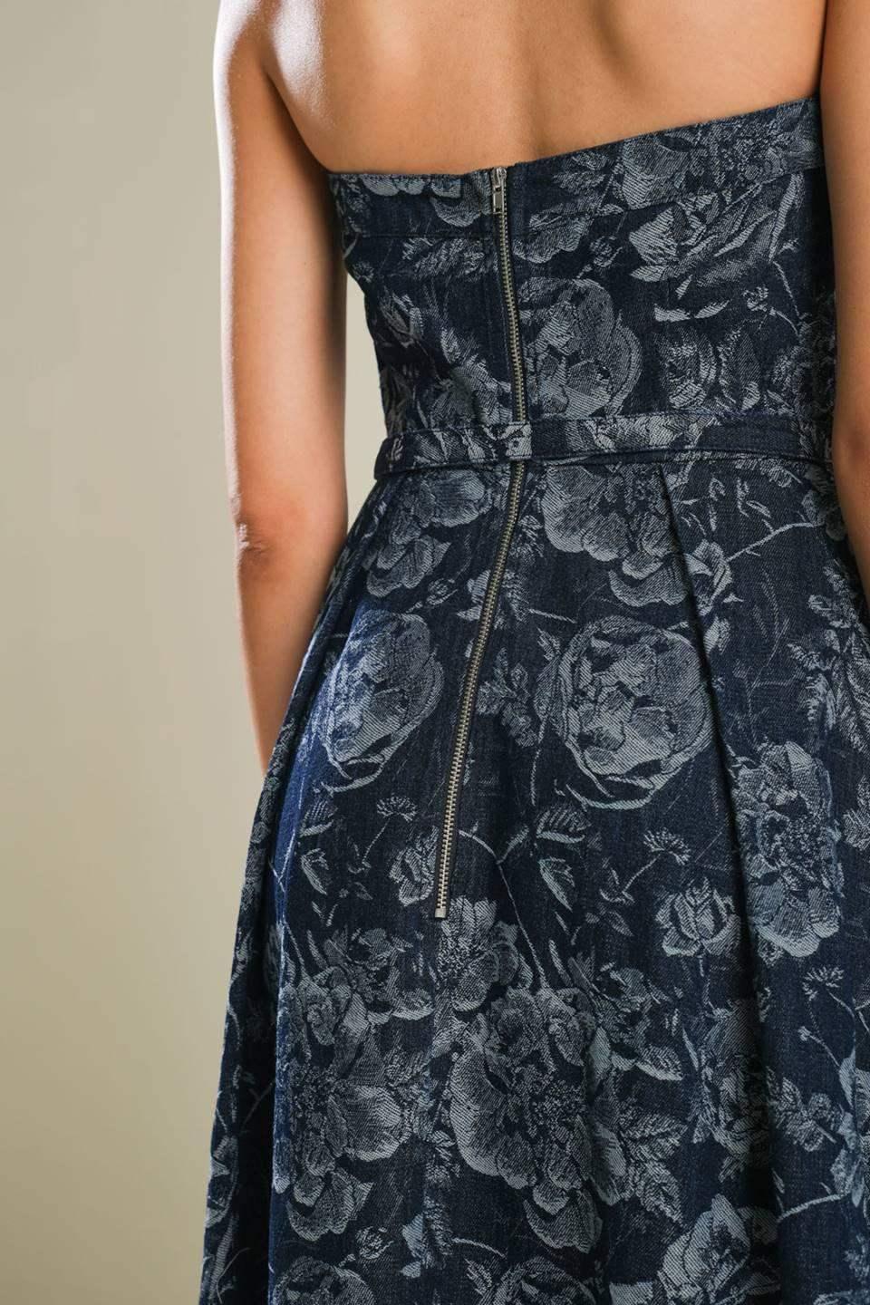 A strapless floral denim dress is displayed, featuring a fitted bodice and a flared skirt, with a visible zipper detail at the back against a neutral backdrop.