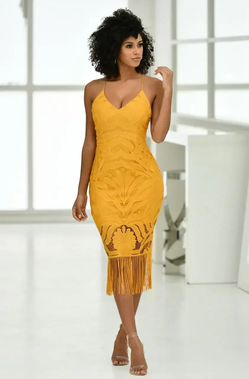 A model stands confidently, showcasing a yellow fringe dress. She poses in a bright, modern setting with large windows, emphasizing the vibrant color and intricate design of her outfit.