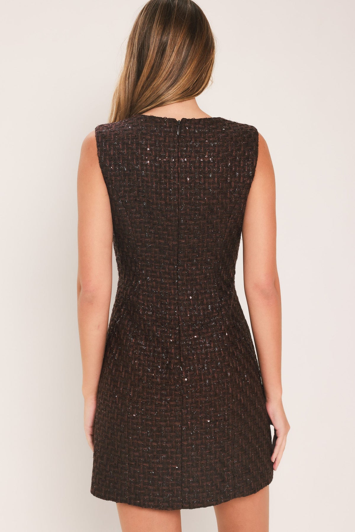 Chocolate Muse Tweed Mini Dress | Lady Black Tie | A woman modeling a sleeveless dark brown tweed mini dress with floral embellishments