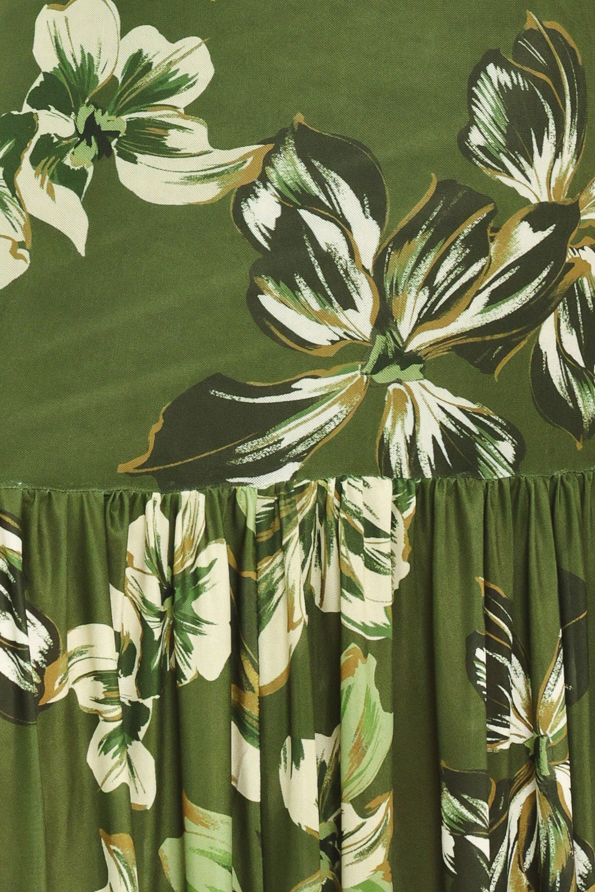 Close-up of a green floral fabric with large white and olive-toned tropical flowers and a gathered ruffled hem.