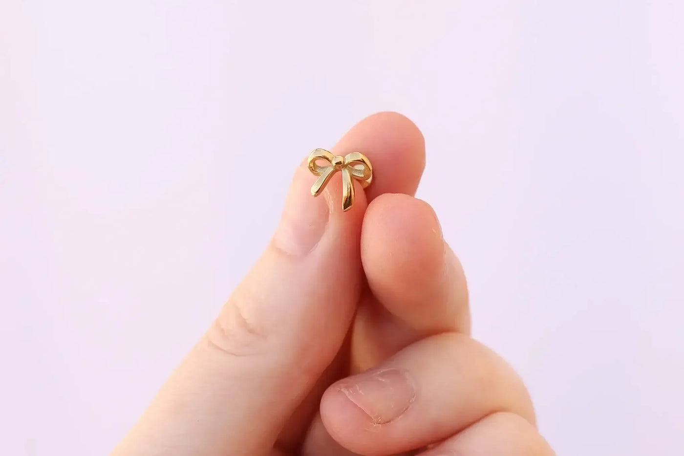A person holds a small gold bow with their fingertips. The background is soft and light, creating a gentle, elegant atmosphere around the delicate object.
