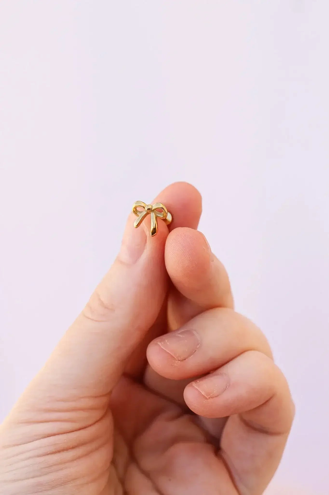 A hand holds a small, shiny yellow bow-shaped object, showcasing its delicate structure against a soft, pastel background. The fingers gently support the item, emphasizing its size.