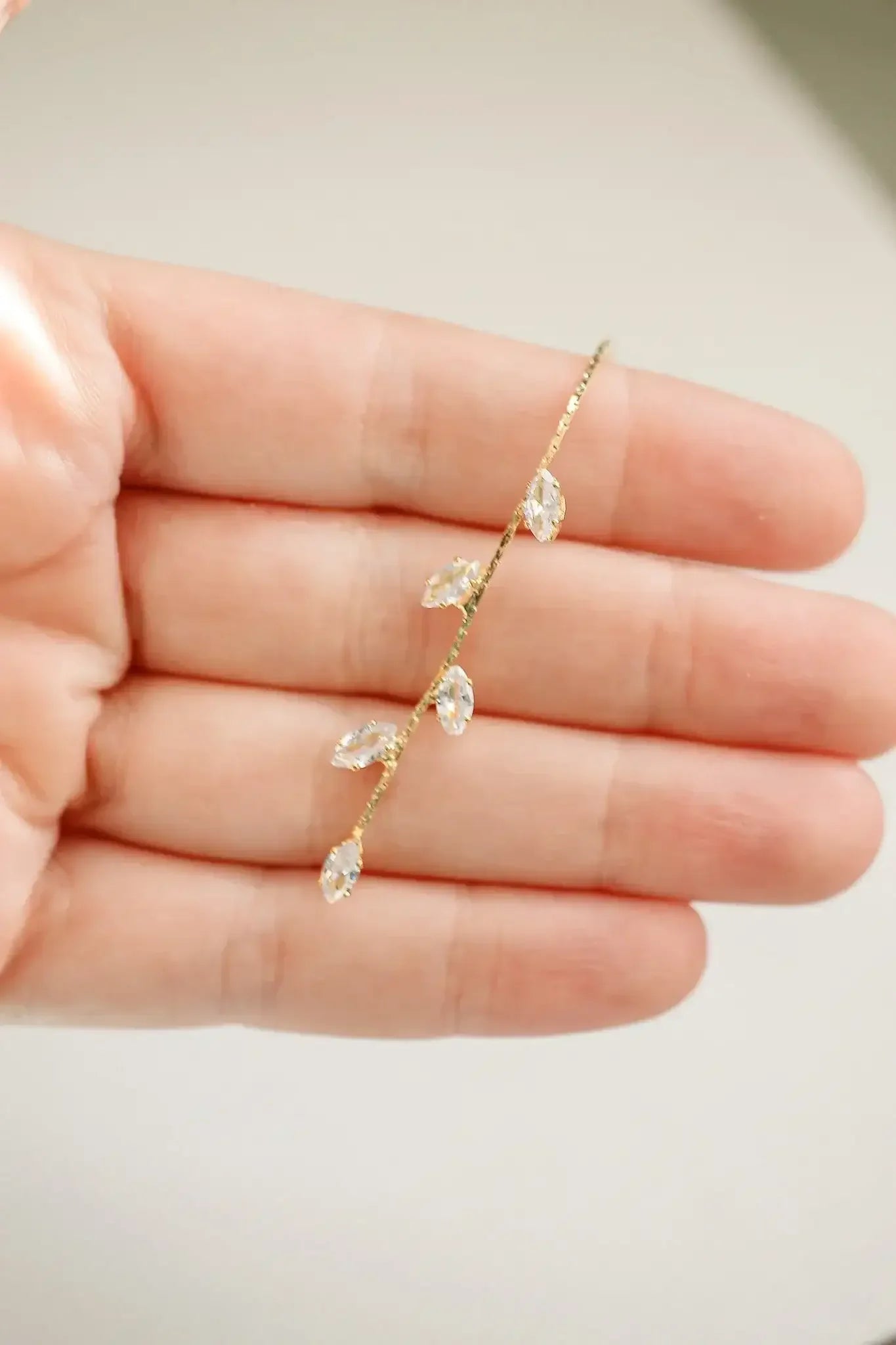A hand holds a delicate hairpin shaped like a branch, adorned with sparkling leaf-like crystals. The background is softly blurred, emphasizing the intricate design of the accessory.