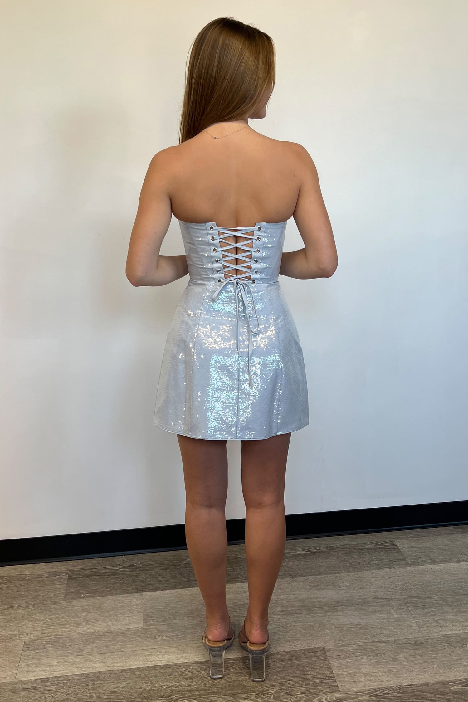 Woman wearing a strapless silver sequin dress against a white wall.