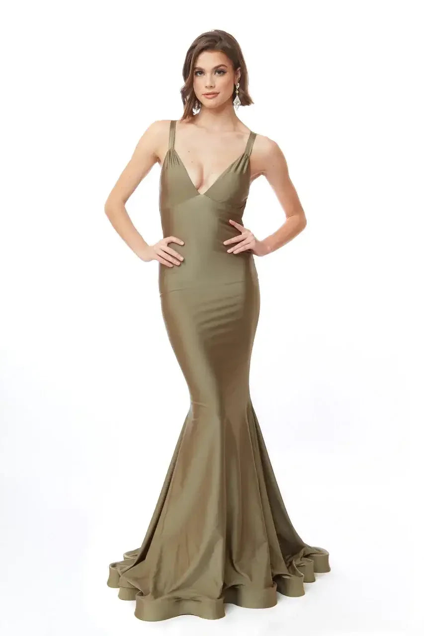 A woman stands confidently in a fitted olive green gown with a mermaid silhouette. She poses with hands on her waist against a plain white background, showcasing elegance and style.