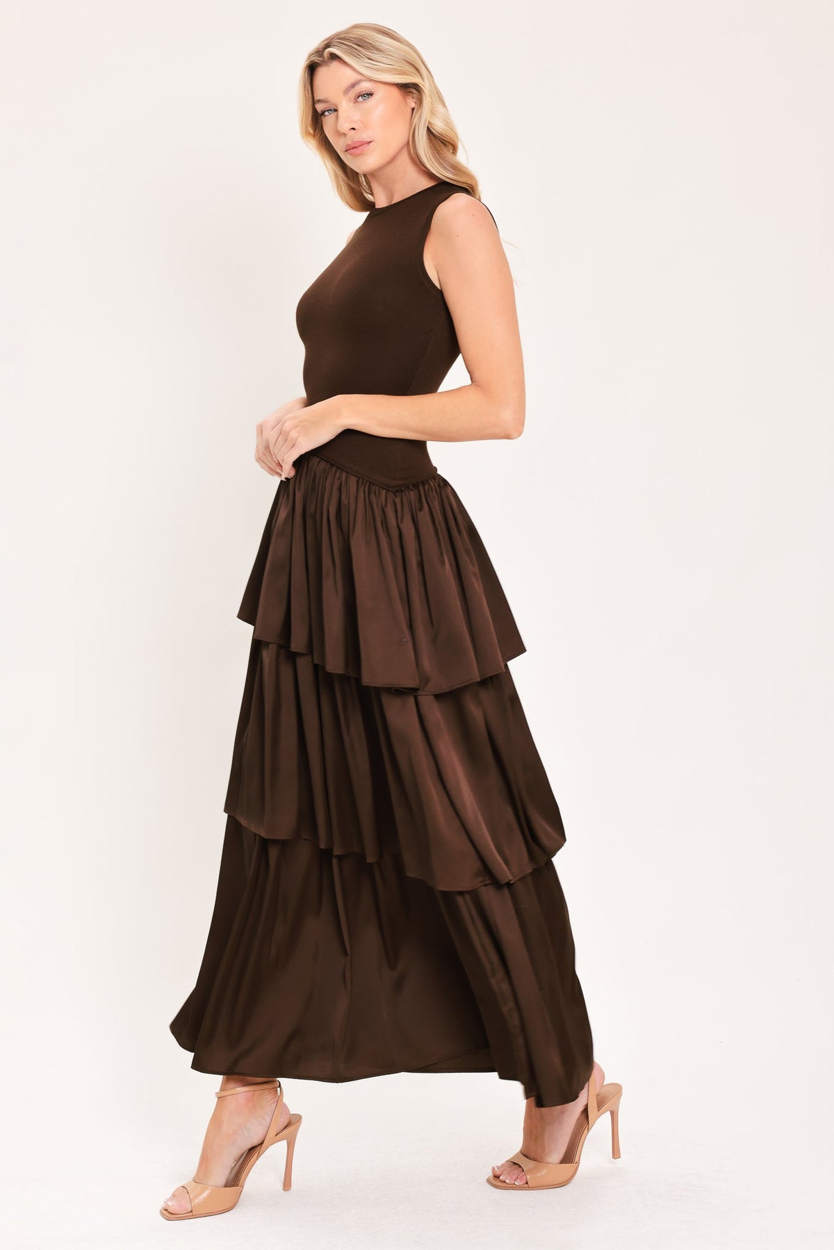 Cocoa Cascade Drop Waist Midi Dress | Lady Black Tie | A woman modeling a sleeveless dark brown dress with a fitted bodice and a tiered maxi skirt