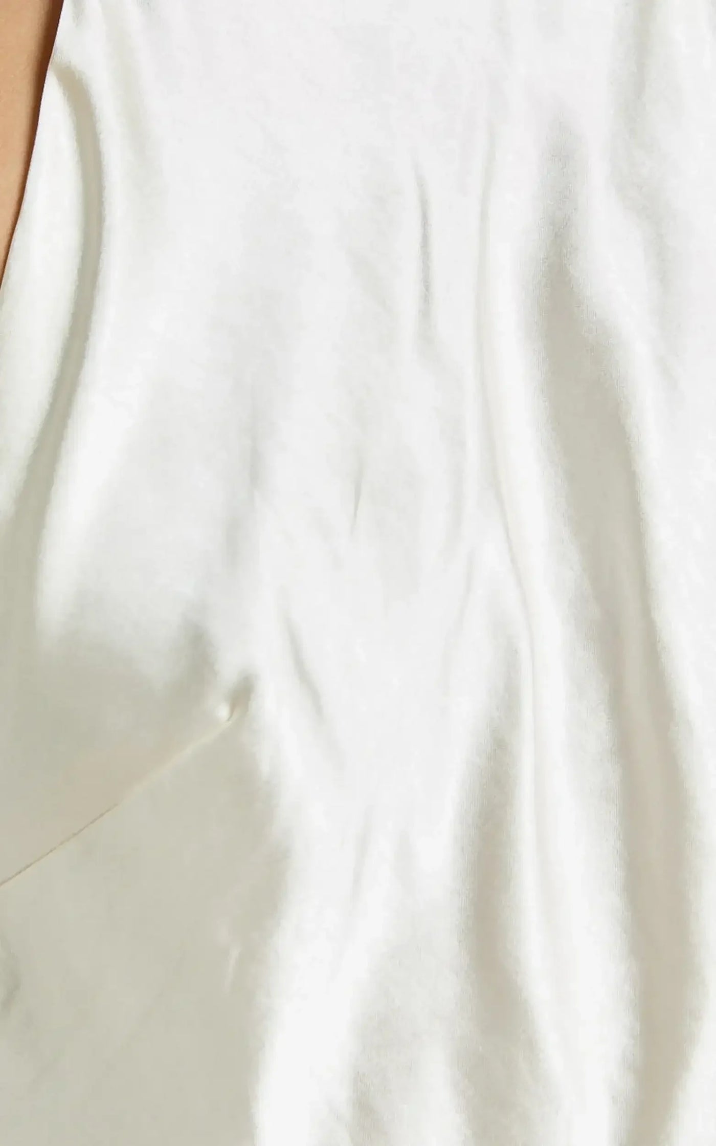 A white fabric drapes softly, displaying gentle folds and textures. Its smooth surface suggests lightweight material, positioned against a neutral background that enhances its simplicity and elegance.