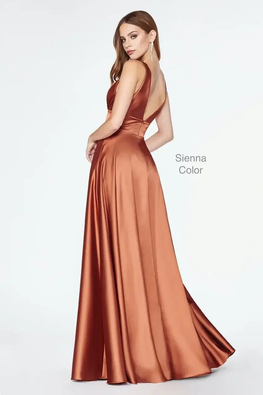 A woman models an elegant, floor-length gown with a deep back and smooth satin fabric in a sienna color, posing confidently against a light backdrop.