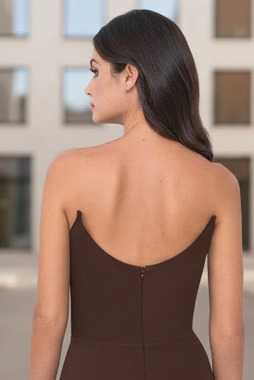 A woman wearing a black, strapless dress stands with her back turned, showcasing the dress's fitted silhouette and zipper detail against a plain white background.