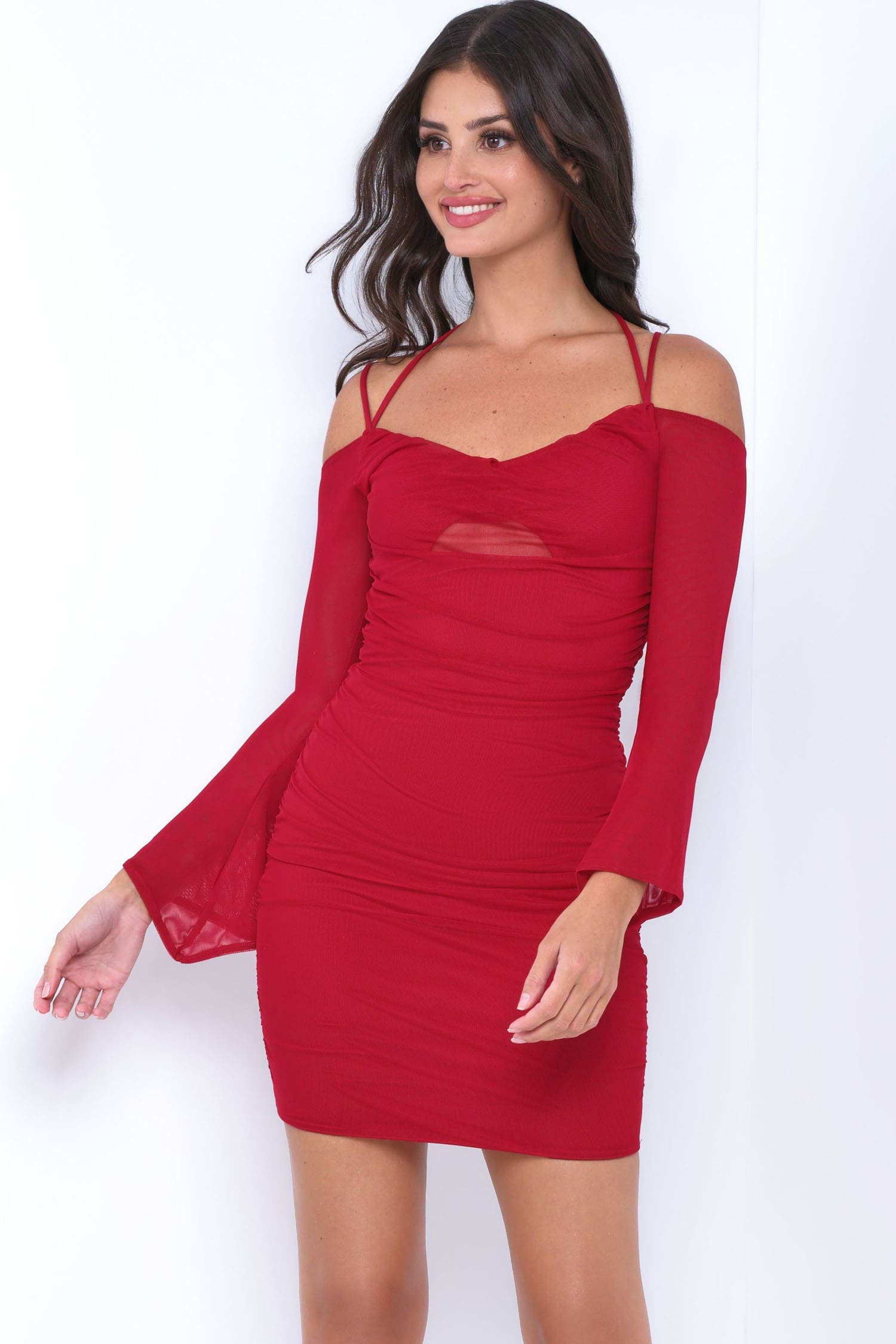 A woman modeling a red off-the-shoulder mini dress with long sheer bell sleeves and a ruched bodice, photographed against a plain white studio background.