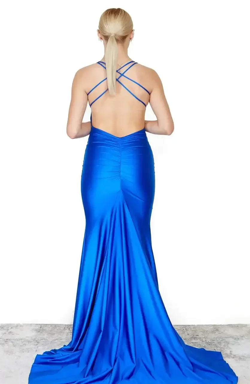 A formal, fitted blue gown with a deep back and crisscross straps drapes elegantly down, blending into a smooth, light-colored floor and white wall backdrop.
