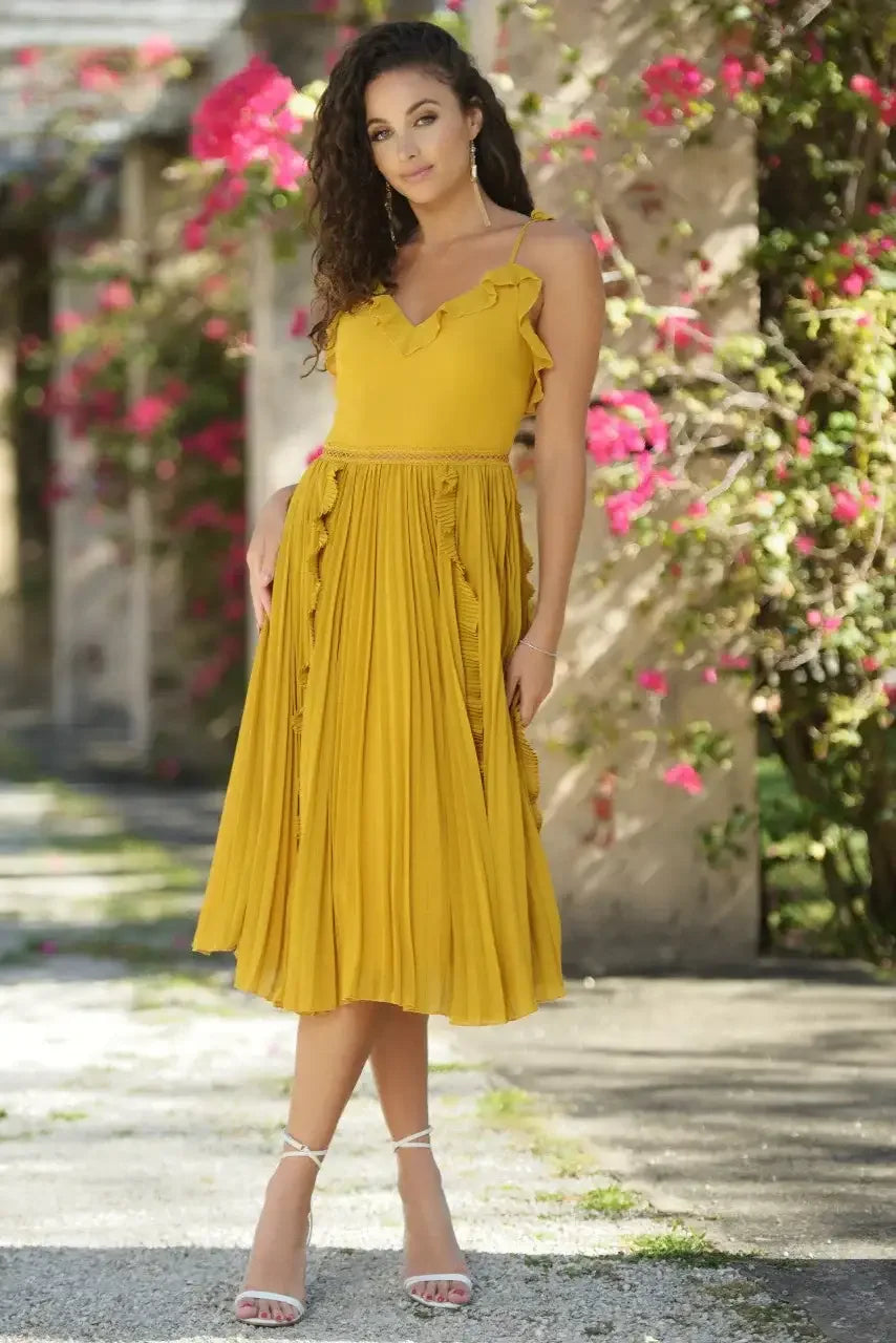 A woman in a flowing yellow dress stands confidently outdoors, surrounded by blooming pink flowers and stone structures, showcasing a vibrant, sunny atmosphere.