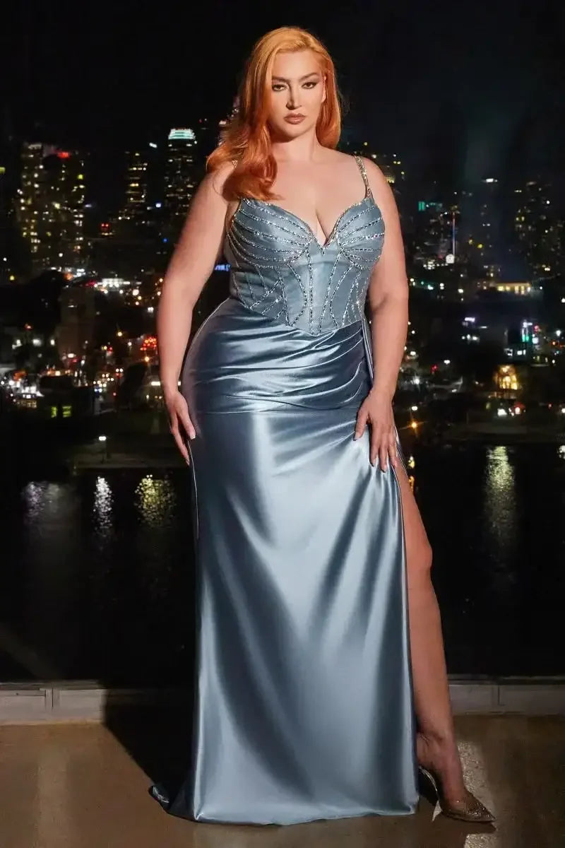 A woman in a shimmering blue evening gown stands confidently, showcasing a high slit. The city skyline glows behind her, indicating a glamorous night setting.