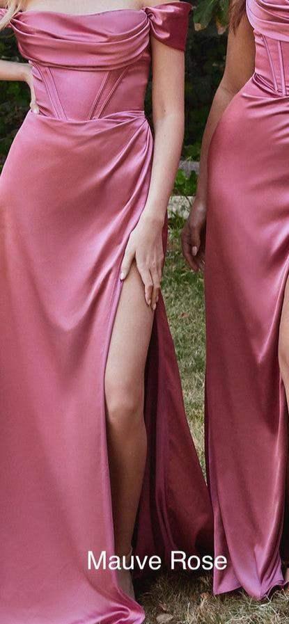 Three women pose in elegant, flowing gowns with high slits, showcasing vibrant colors: mauve rose and mauve. They stand in a lush garden setting, surrounded by greenery.