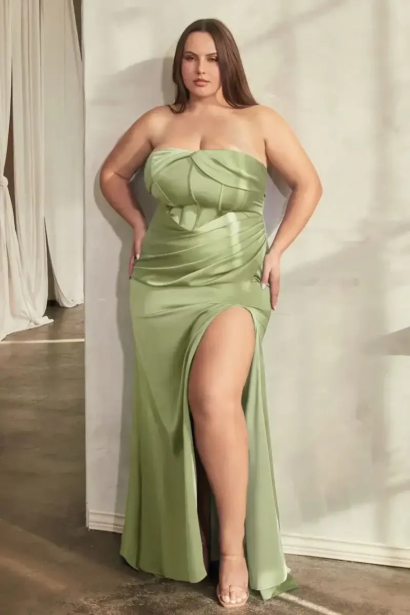 A woman in a strapless, flowing, light green dress with a slit poses confidently against a textured wall. Soft lighting creates a warm, elegant atmosphere.