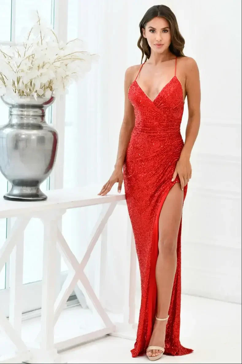 A woman in a dazzling red sequined gown poses confidently beside a silver vase filled with white flowers, set against a bright, minimalist interior with white walls and large windows.