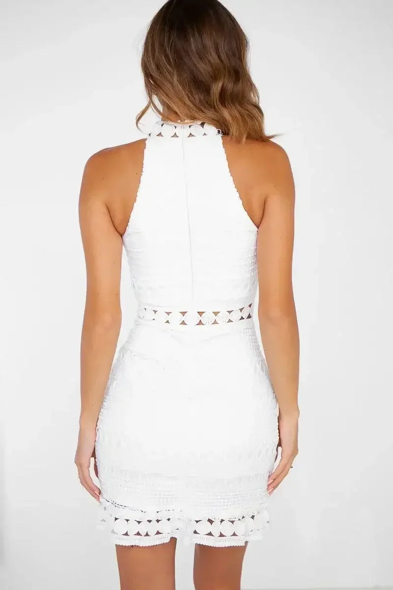 A white halter dress with intricate patterns and lace hem is worn by a woman, showcasing her back. The background is plain, emphasizing the dress's details.
