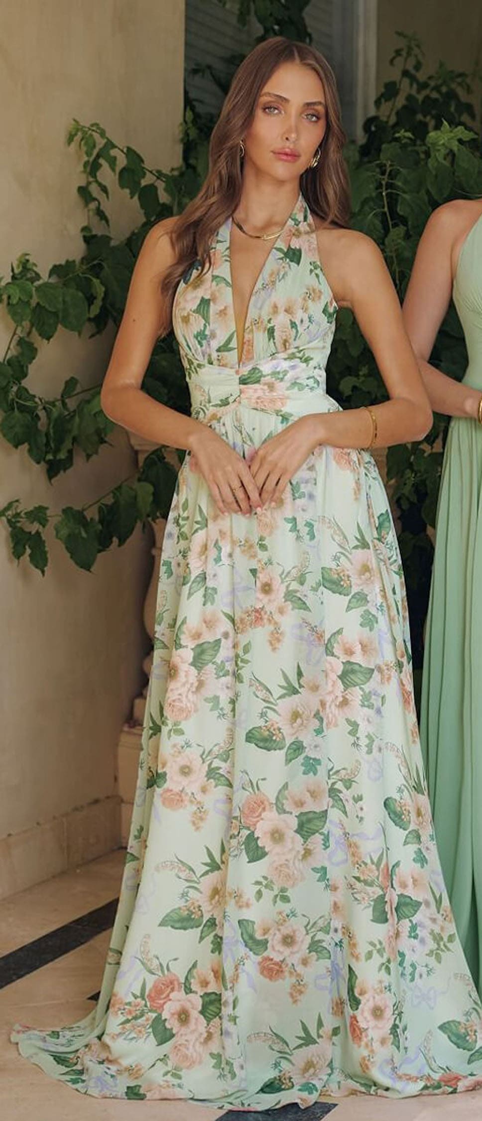 Woman wearing a floral dress standing outdoors with greenery in the background