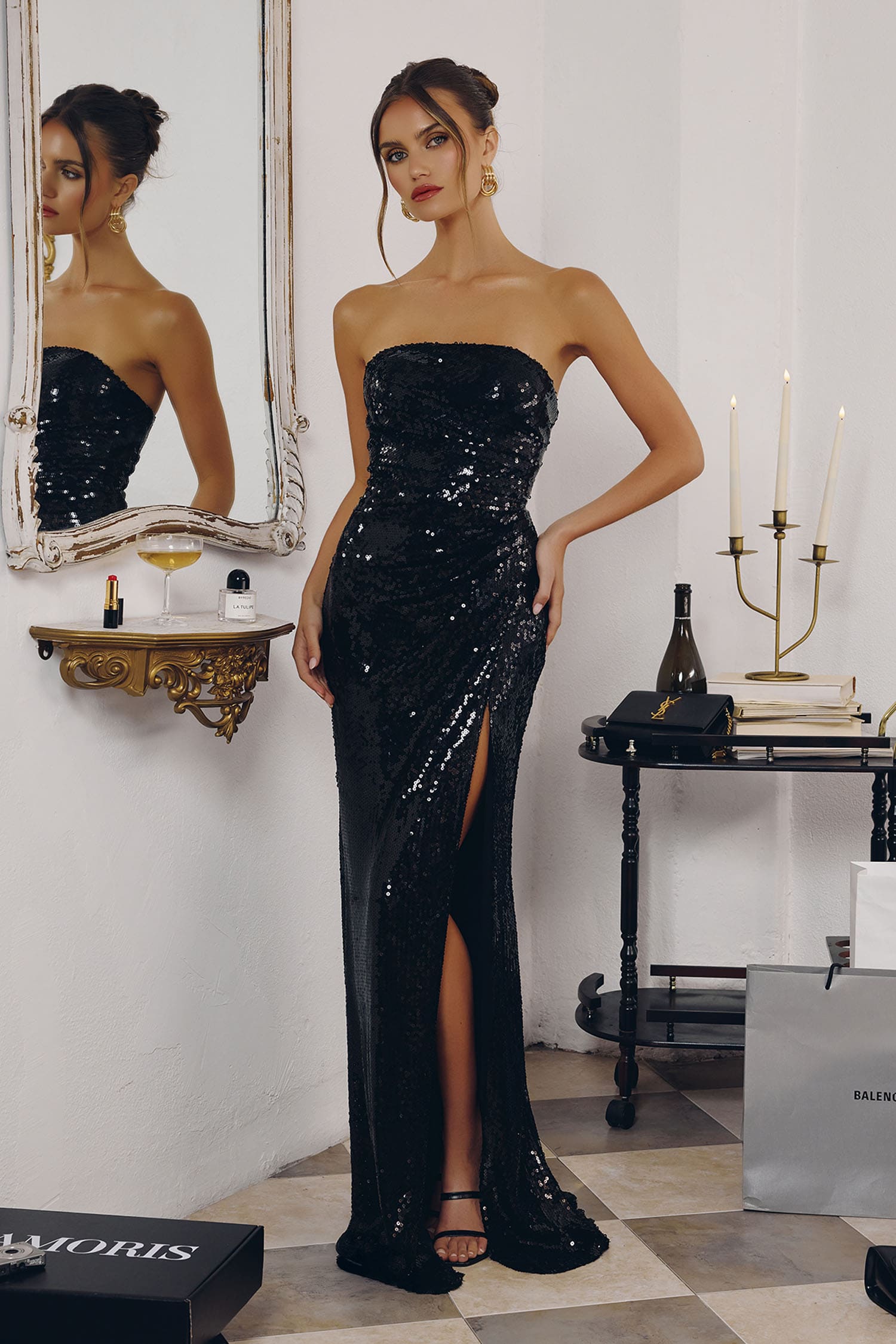 Woman in a black sequin gown standing in a room with a mirror and candles.