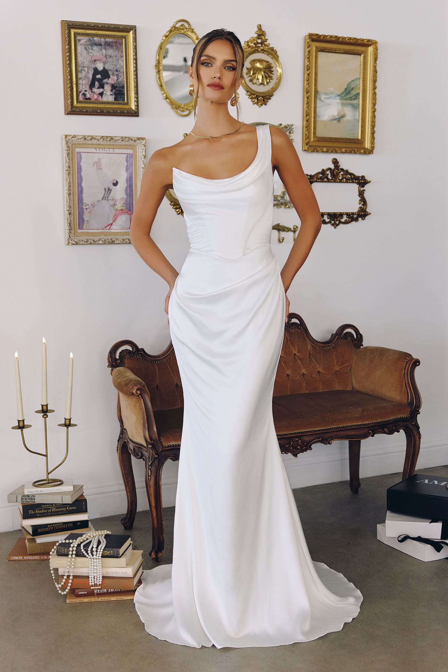 Woman in a white dress standing in a room with decorative wall art and furniture.