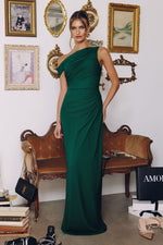 Woman in a green one-shoulder dress standing in a room with vintage decor.