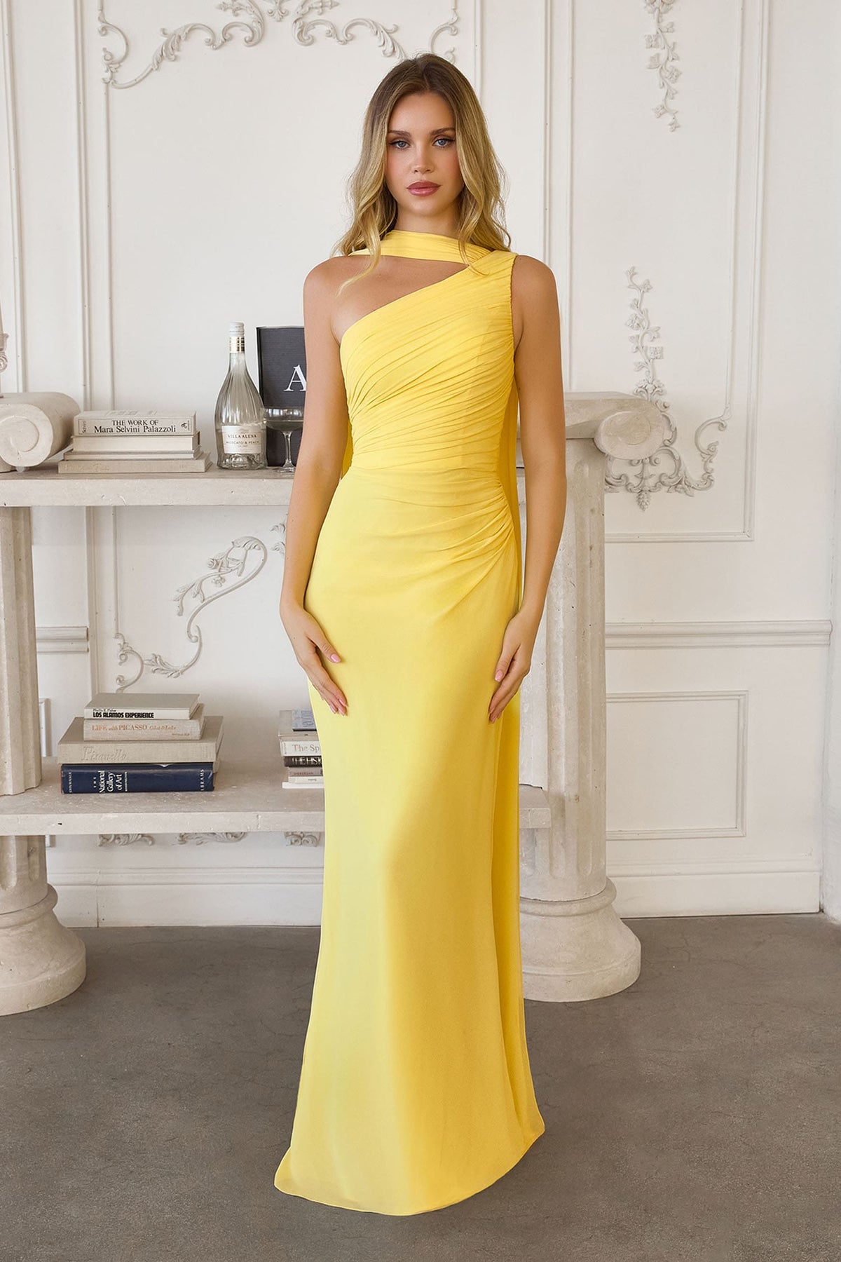 Woman wearing a yellow one-shoulder dress in an elegant room.